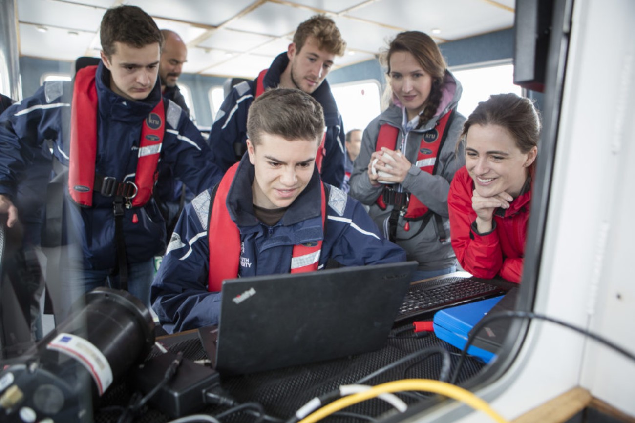 A team of young people look at underwater technology data on a screen