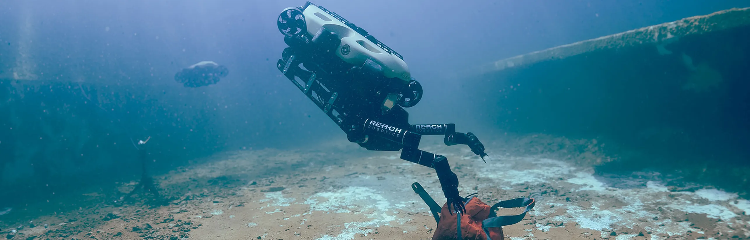 SRS ROV with Reach Robotics arms unzipping a bag on the seabed